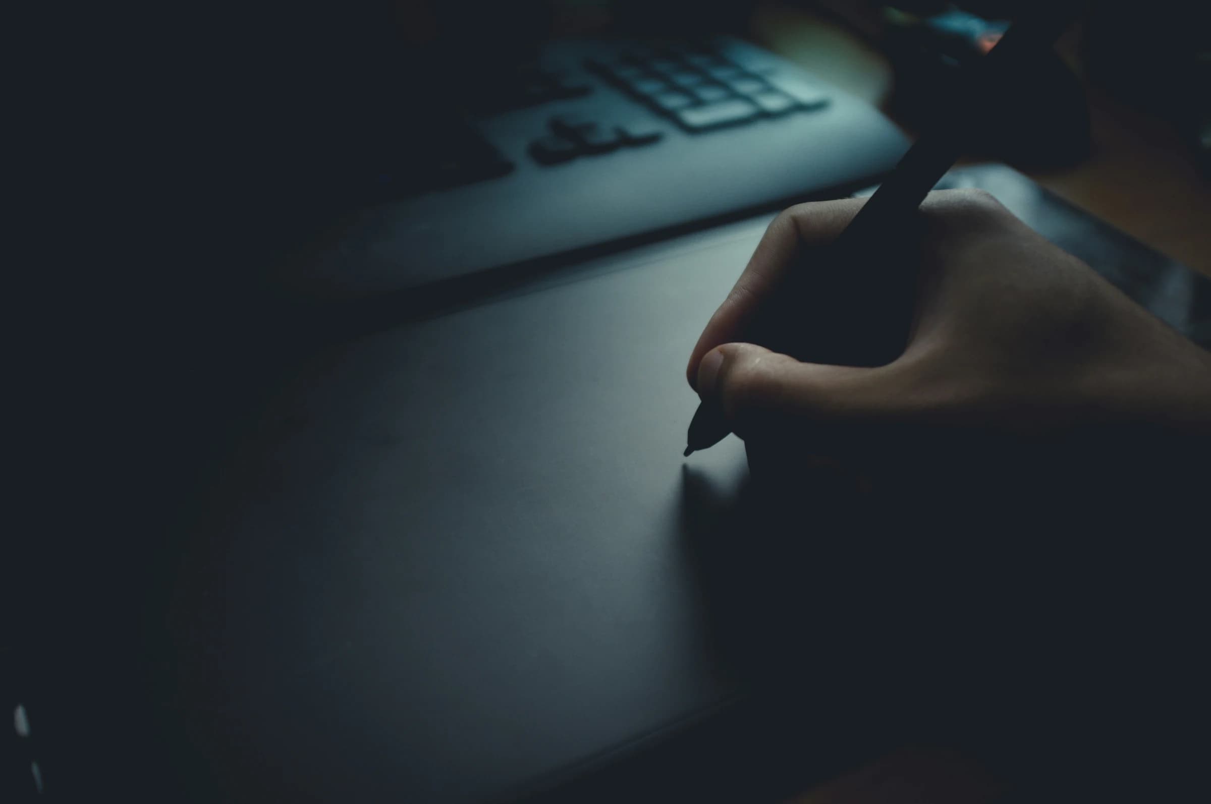 A designer's hand drawing with a stylus on a graphics tablet in a dark room