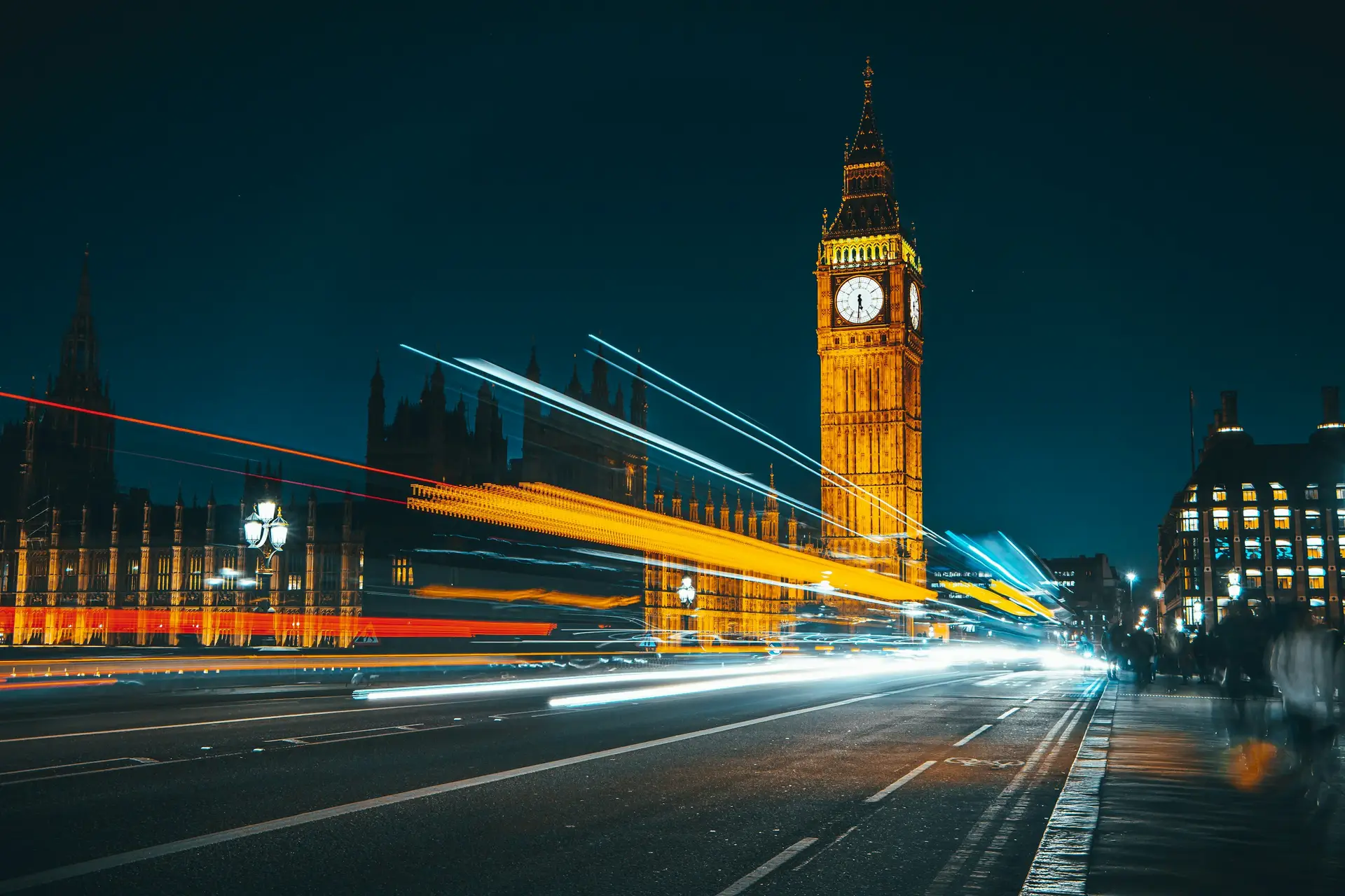 The Elizabeth Tower and the Palace of Westminster lit at night, with traffic light trails across Westminster Bridge