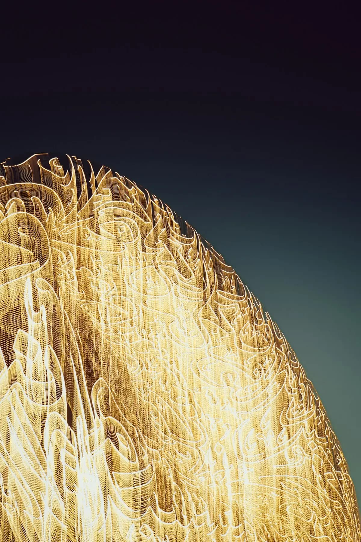 A curved structure covered in lit golden Arabic calligraphy against a dark night sky