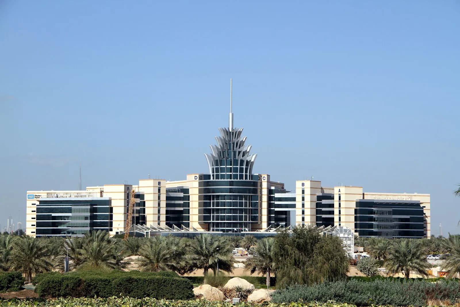 The Dubai Silicon Oasis headquarters building, with its spired central tower, seen across a line of palm trees